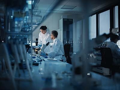 Two scientists in a laboratory having a discussion while looking into a microscope
